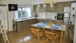 A modern kitchen with a dining area, featuring a large island, built-in appliances, and a television mounted on the wall. - Mpoulakis Apt 46, 3 bedroom family apartment next to my photo studio (Κίσσαμος)