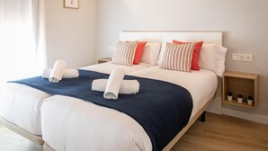 A neatly made bed with white and navy blue bedding, two pillows with striped patterns, and two rolled white towels. There are bedside tables with small potted plants and a power outlet on the wall. - 1.2 New & stylish flat   Barcelona Touch Apartments (Barcelona)