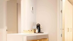 A modern kitchen with a white countertop, wooden stools, and a coffee machine.