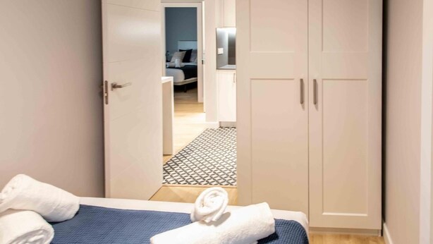 A bedroom with a bed, two towels, a wardrobe, and a hallway leading to a bathroom.