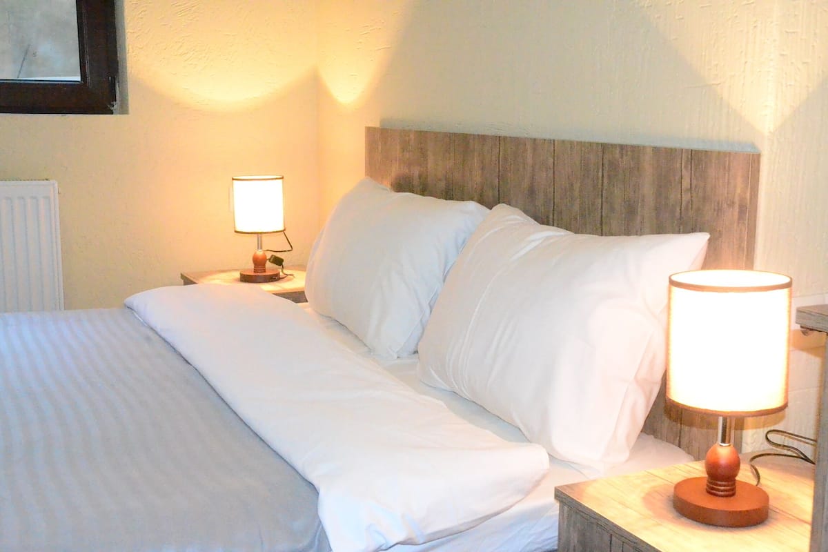 A neatly made bed with white linens, a wooden headboard, and a nightstand with a lamp.