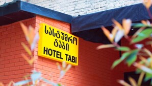 A yellow sign with "HOTEL TABI" written in English and another language, mounted on a red brick wall. - Hotel Tabi (Tbilisi)