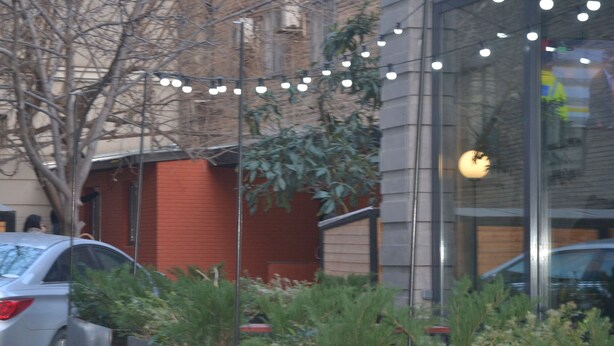 A building with a glass facade, a red brick wall, and a car parked in front. - Hotel Tabi (Tbilisi)