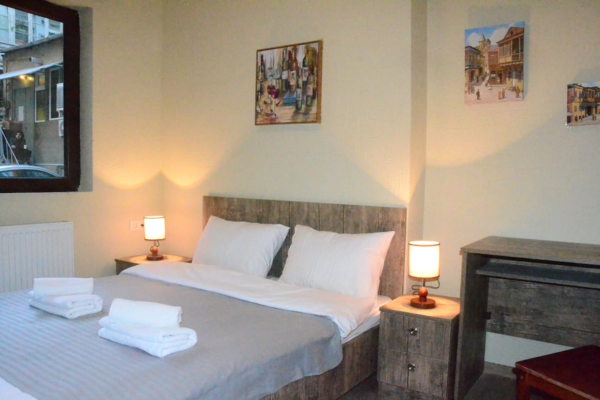 A hotel room with a bed, two bedside tables with lamps, a wooden dresser, and artwork on the walls.
