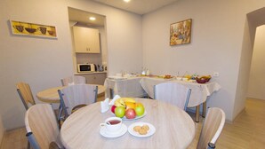 A dining area with round tables, chairs, a microwave, and a buffet table with food and drinks. - Hotel Tabi (Tbilisi)