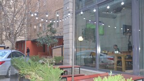 An outdoor seating area with benches and potted plants, a car parked nearby, and a building with large windows reflecting interior lighting. - Hotel Tabi (Tbilisi)
