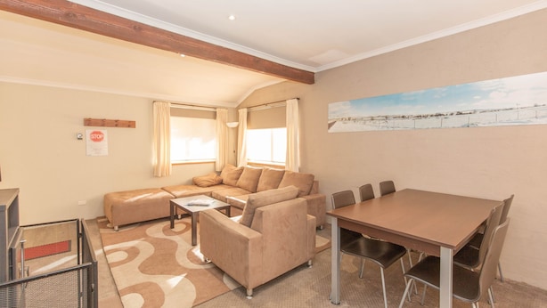 Un salon chaleureux avec un canapé d’angle, une table à manger avec des chaises et un tableau représentant un paysage enneigé.