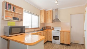 Une cuisine compacte avec des meubles en bois, un four à micro-ondes encastré, une cuisinière et une fenêtre équipée de stores.