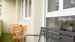 A balcony with a black bench, orange chairs, and a small table.