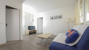 A modern living room with a sofa, a TV on a wooden stand, a table, and a lamp.
