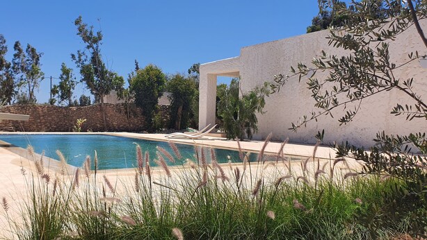 A swimming pool with a stone wall and a white structure in the background. - Unique Architect's House (Ghazoua)