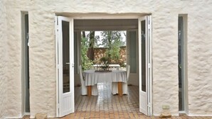 An open doorway leading to a covered patio area with a table set for dining. - Unique Architect's House (Ghazoua)