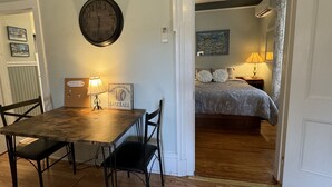Una habitación con una mesa de comedor de madera y sillas, un reloj de pared, un letrero con temática de béisbol y una cama con colcha estampada.