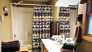 A bathroom with a shower curtain featuring animal prints, a sink with toiletries, and towels stacked on a wooden shelf.