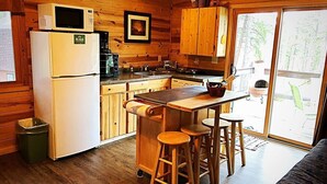 A compact kitchen with wooden cabinets, a refrigerator, a microwave, and a bar stool area.
