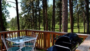 Una terraza con mesa y sillas, una parrilla y vistas a un bosque.