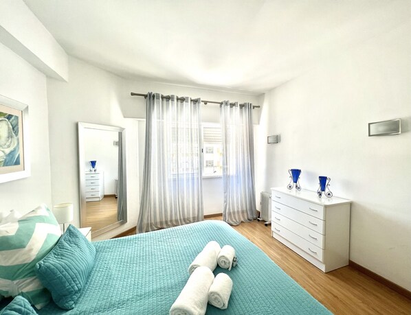 A bedroom with a bed, a dresser, a mirror, and a window with curtains.