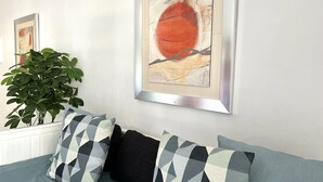 Ein Zimmer mit einer Couch, zwei gemusterten Kissen, einer Pflanze und zwei abstrakten Bildern an der Wand.