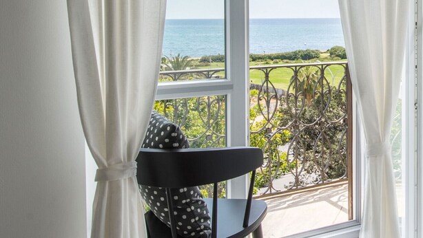 Ein Balkon mit Meerblick, einem Stuhl und weißen Vorhängen.