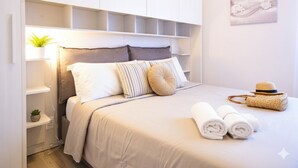 A neatly arranged bedroom with a bed, pillows, a bedside table with a plant, and a wall-mounted shelf. - Casa di Luigi ed Ernestina (Dolcedo)