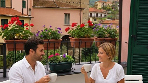 A couple dining at an outdoor table with a view of buildings and flowers. - Casa di Luigi ed Ernestina (Dolcedo)