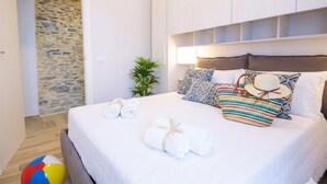 A bedroom with a stone wall, a bed with white linens, colorful pillows, and a beach ball. - Casa di Luigi ed Ernestina (Dolcedo)