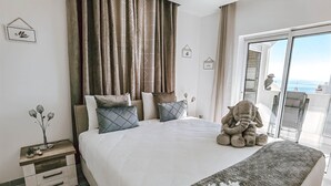 A bedroom with a large bed, a nightstand, a plush elephant toy, and a view of the sea through a sliding door. - Apartment Dubai, Sea View - Praia da Rocha   (Portimão)