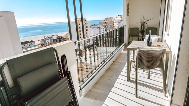 A balcony with a view of the beach and cityscape, a table with chairs, and a plant. - Apartment Dubai, Sea View - Praia da Rocha   (Portimão)
