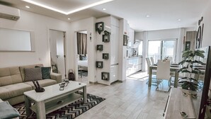 A modern living room with a sofa, coffee table, and a dining area with chairs and a table. - Apartment Dubai, Sea View - Praia da Rocha   (Portimão)