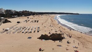 A wide sandy beach with rows of umbrellas and sunbeds, a rocky outcrop, and a clear blue sky. - Apartment Dubai, Sea View - Praia da Rocha   (Portimão)