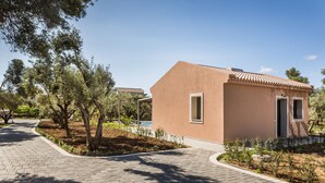 A building with a flat roof and a small entrance door, surrounded by a paved walkway and trees. - VILLA LAURA (Svoronata, Kefalonia)