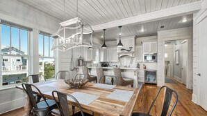 Un vaste espace dédié à la salle à manger, avec une table et des chaises en bois, un lustre et une vue sur l’extérieur.