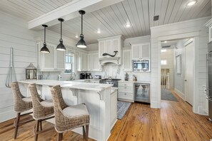 Cocina con armarios blancos, una isla central con taburetes y luminarias colgantes.