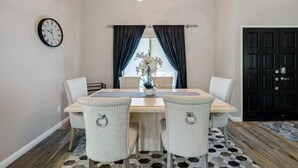 A dining room with a wooden table, four upholstered chairs, a wall clock, a chandelier, and a window with dark curtains. - Santa Rosa Cove #6 , 3 bedroom 2 bath Condo! (La Quinta)