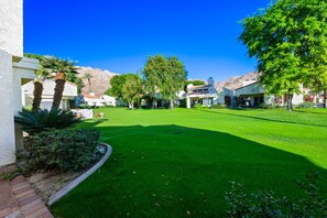 A well-maintained lawn with a clear sky, surrounded by buildings with a Mediterranean architectural style.