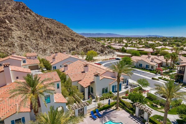 A residential area with terracotta-roofed houses, palm trees, and a mountainous backdrop.