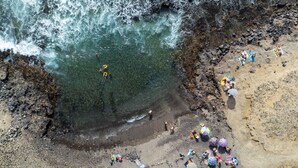 Vista aèria d'una platja rocosa amb aigua cristal·lina, persones i ombrelles.
