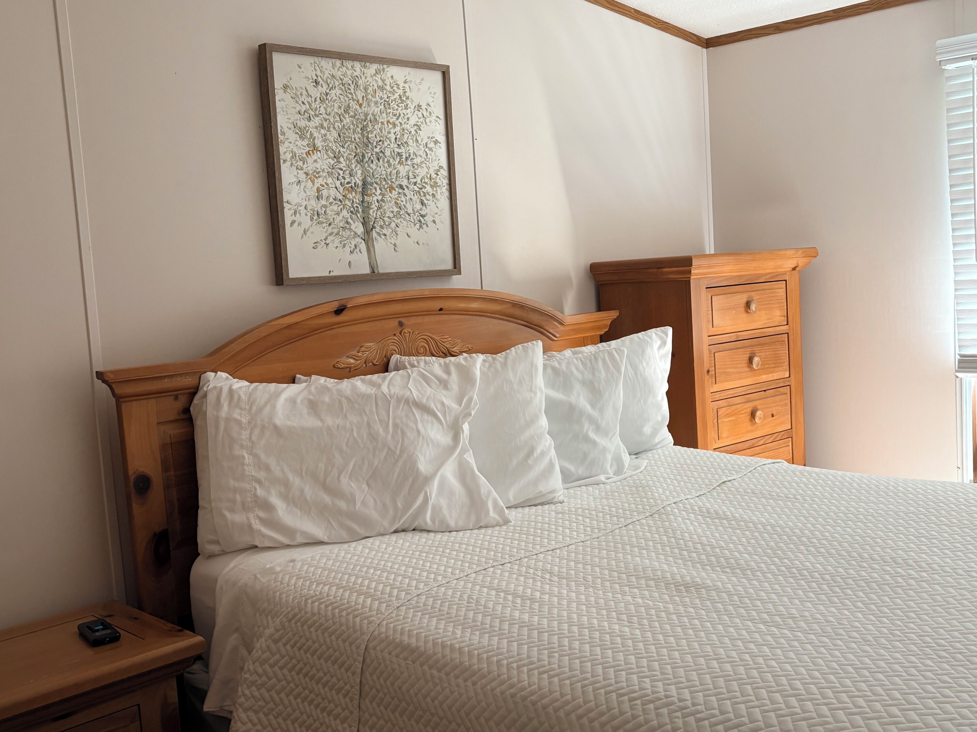 A neatly made bed with a wooden headboard, a bedside table with a phone, and a nightstand.