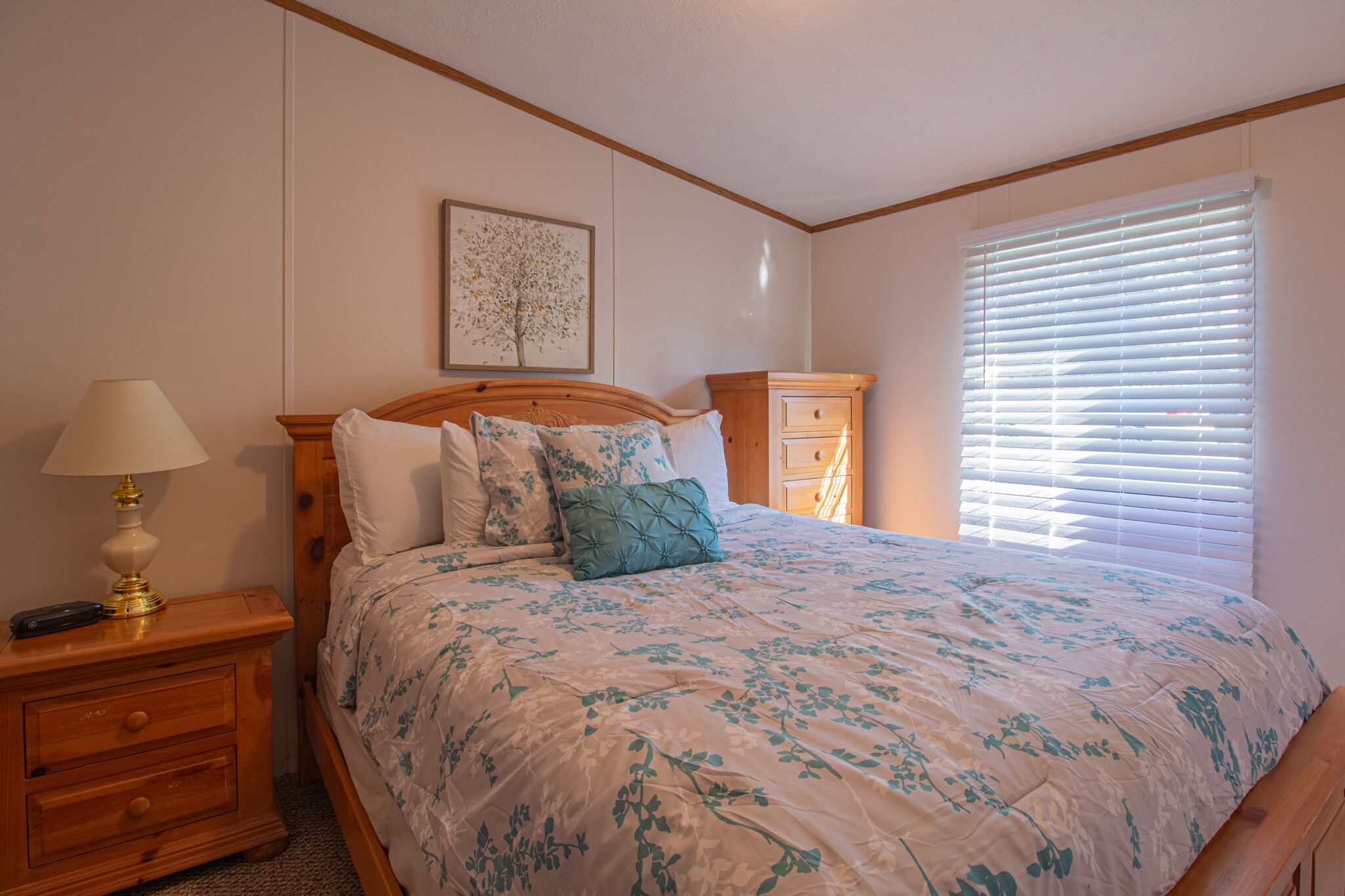 Une chambre à coucher avec un grand lit, une table de chevet avec une lampe, une commode et une fenêtre avec des stores.