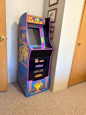 A retro arcade machine with 'Pac-Man' branding, located in a corner of a room with carpeted flooring and wooden doors. - Stay In Ohiopyle next to the GAP Trail (Ohiopyle)