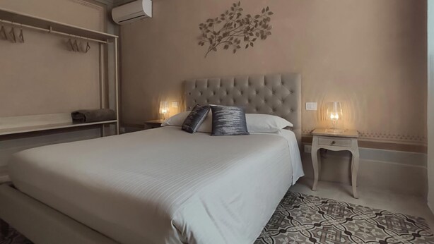 A neatly arranged bedroom with a large bed, a bedside table with a lamp, and a wall-mounted air conditioner. - Lo Strullo Minisuite (Pisa)