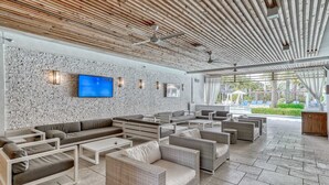 Un espacio lounge moderno al aire libre con disposición de asientos, un televisor de pantalla plana y vistas a una piscina y vegetación.