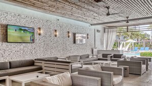 Un área de descanso moderna con pared de piedra, asientos cómodos, televisor de pantalla plana y vista a la piscina.