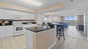 A modern kitchen with white cabinets, a central island, and a dining area with blue chairs. - Yacht Club Villas #1-701 Great Location! (North Myrtle Beach)