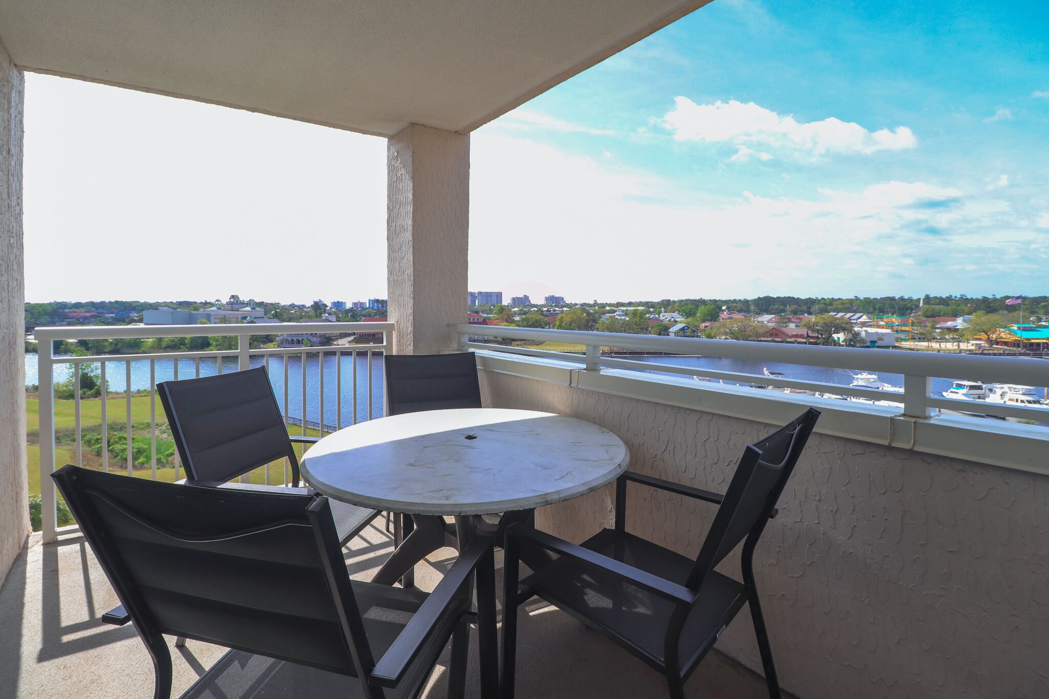 A balcony with a table and chairs, overlooking a body of water and a cityscape.