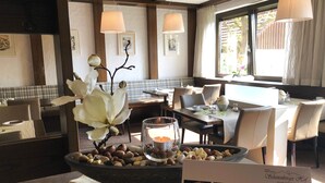 A dining area with a table set for two, a bowl of nuts, a candle, and a framed menu.