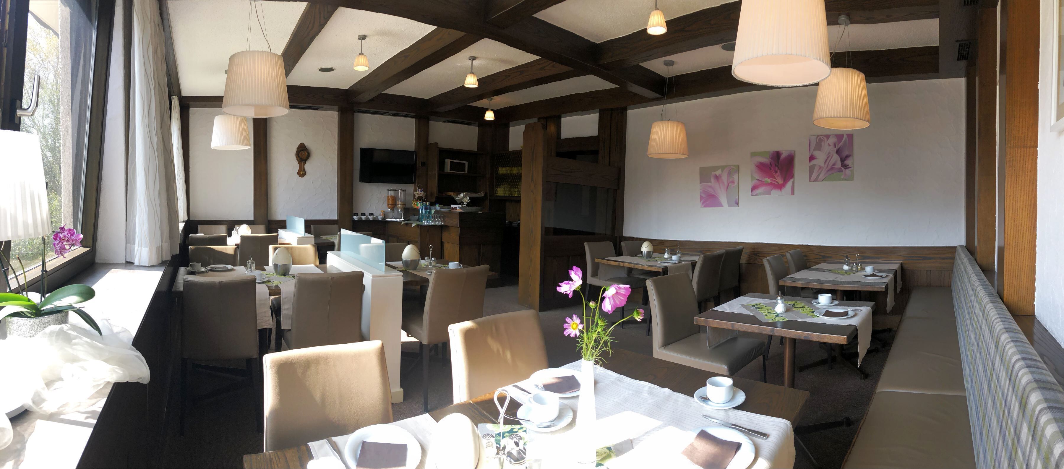 En restaurant med flere borde og stole, et barområde og et stort vindue med gardiner.