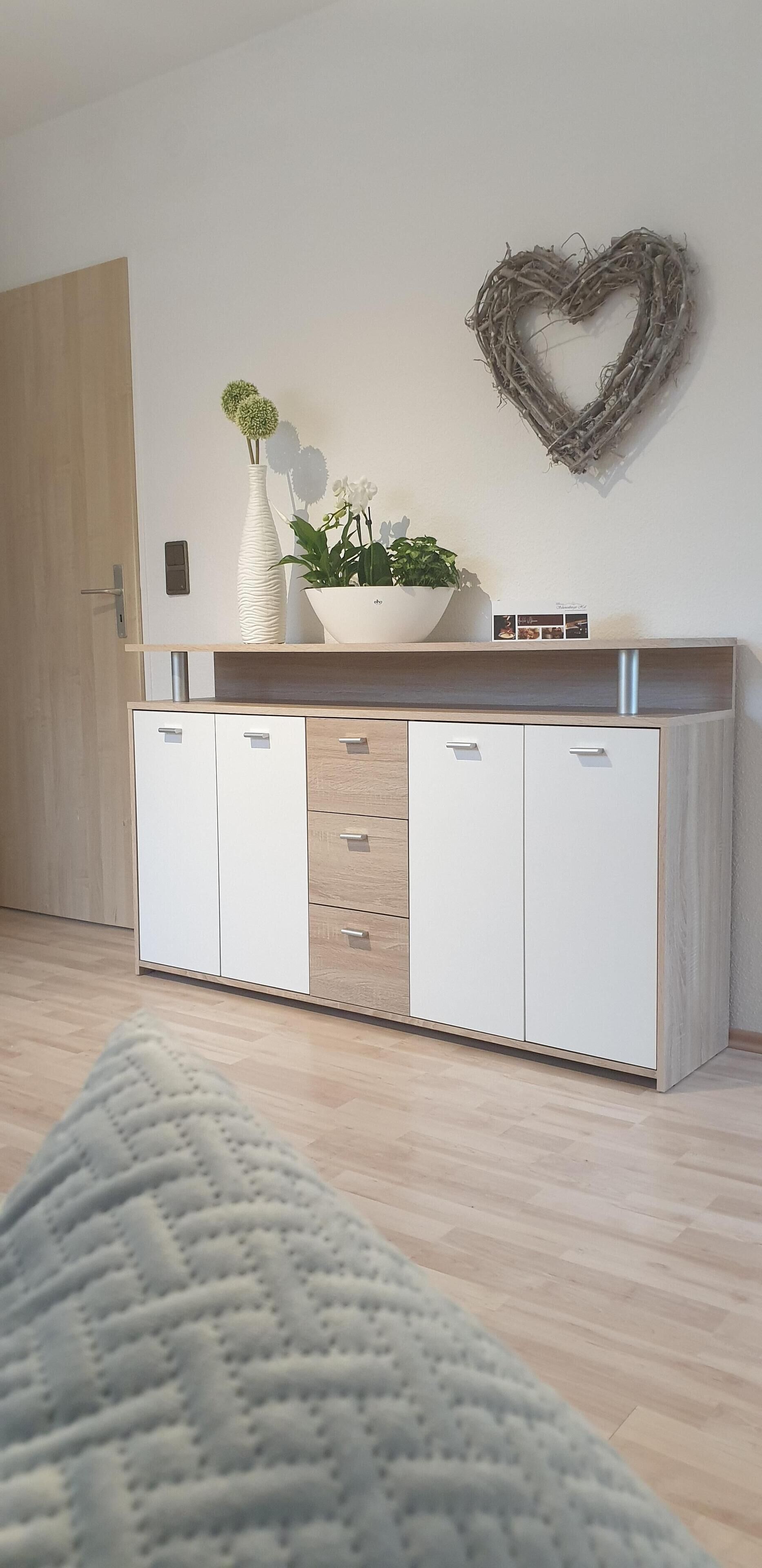 A modern kitchen with a wooden countertop, white cabinets, and a heart-shaped decoration on the wall.