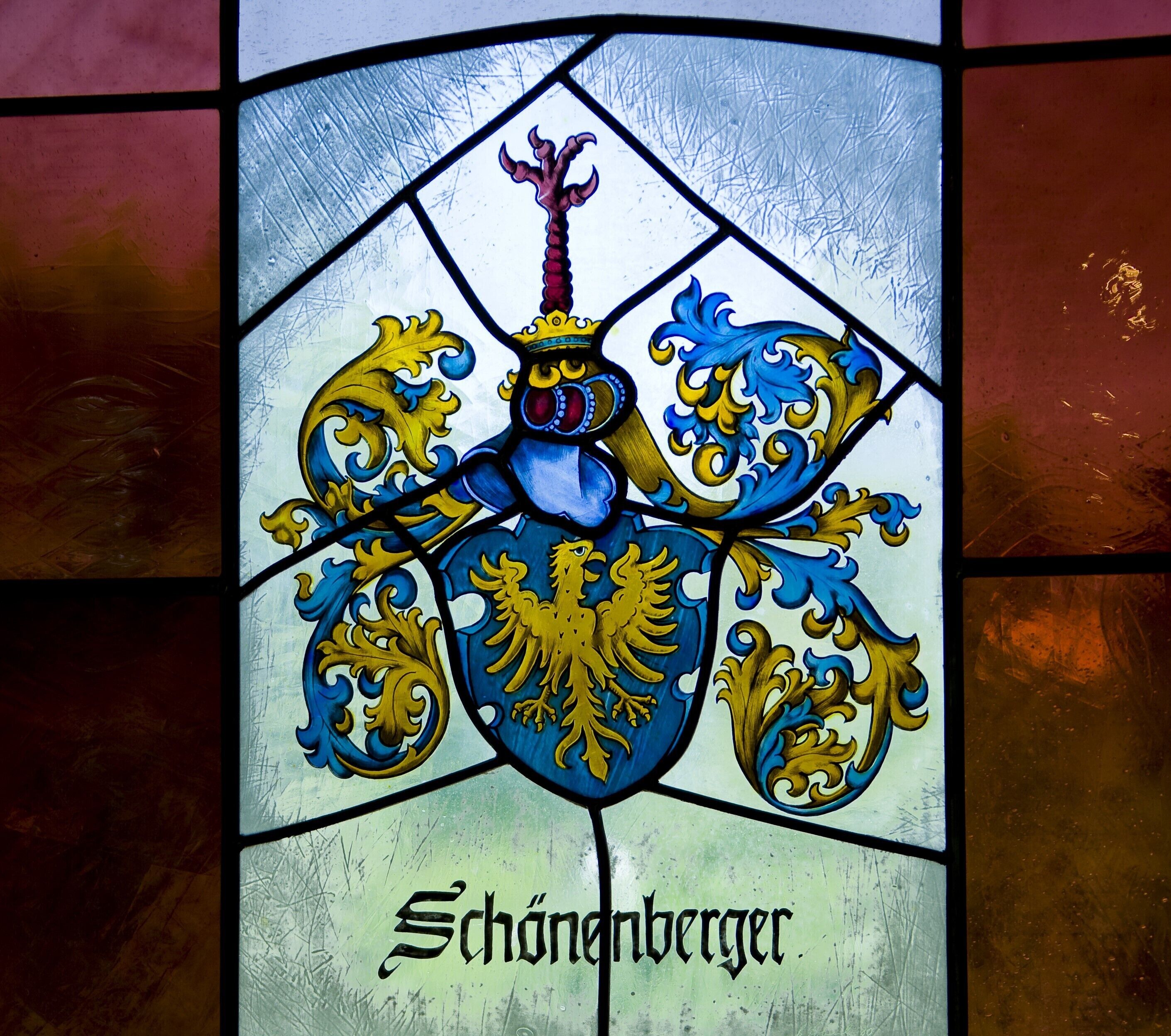 Ein Buntglasfenster mit Wappen und dem Namen "Schönberger".