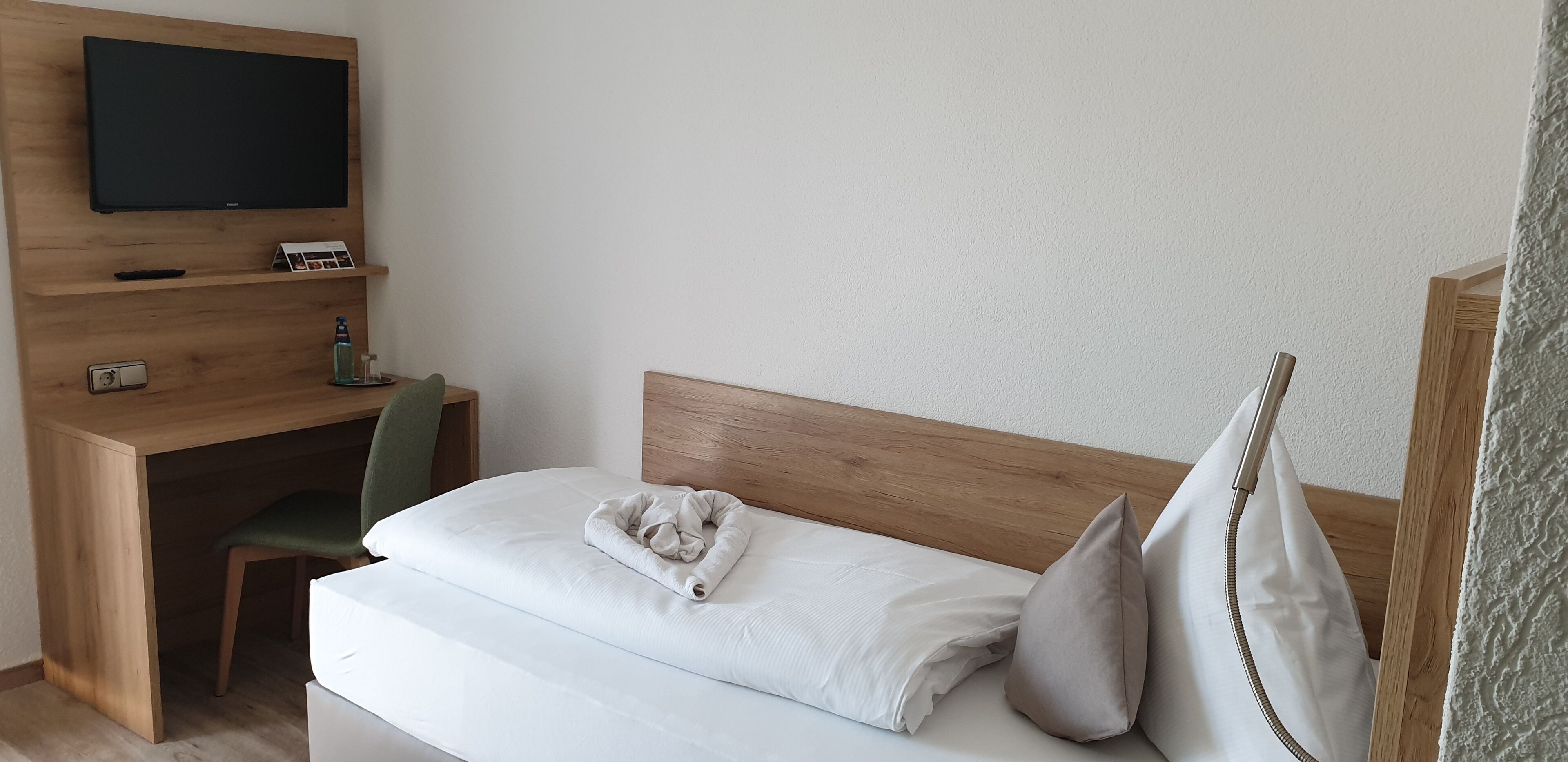 A hotel room with a bed, a desk with a TV, a chair, and a wooden headboard.